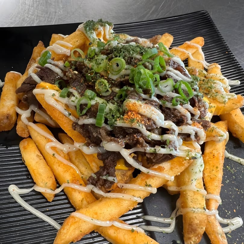 Tonkotsu Ramen Bar's loaded fries with beef, cheese, green onions, and white sauce on a black plate.