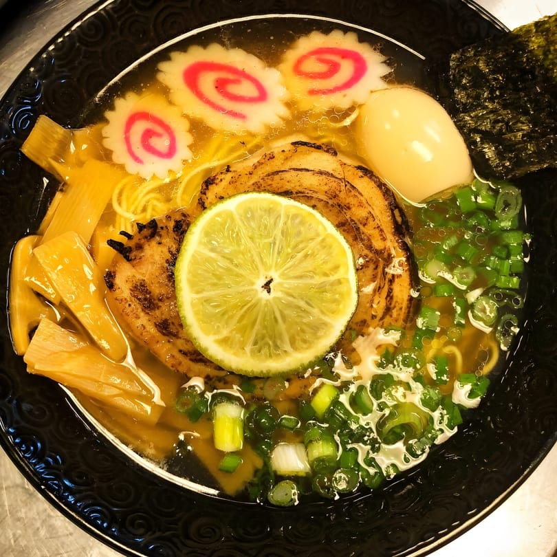 A close-up of Tonkotsu Ramen with pork, egg, lime, scallions, bamboo shoots, and narutomaki.